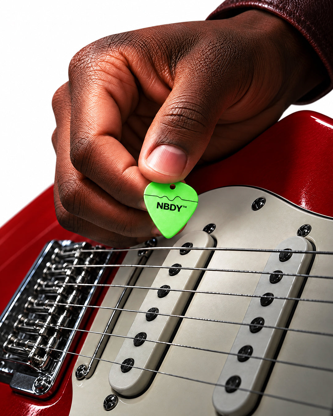 Hand holding a green NBDY pick over a red electric guitar