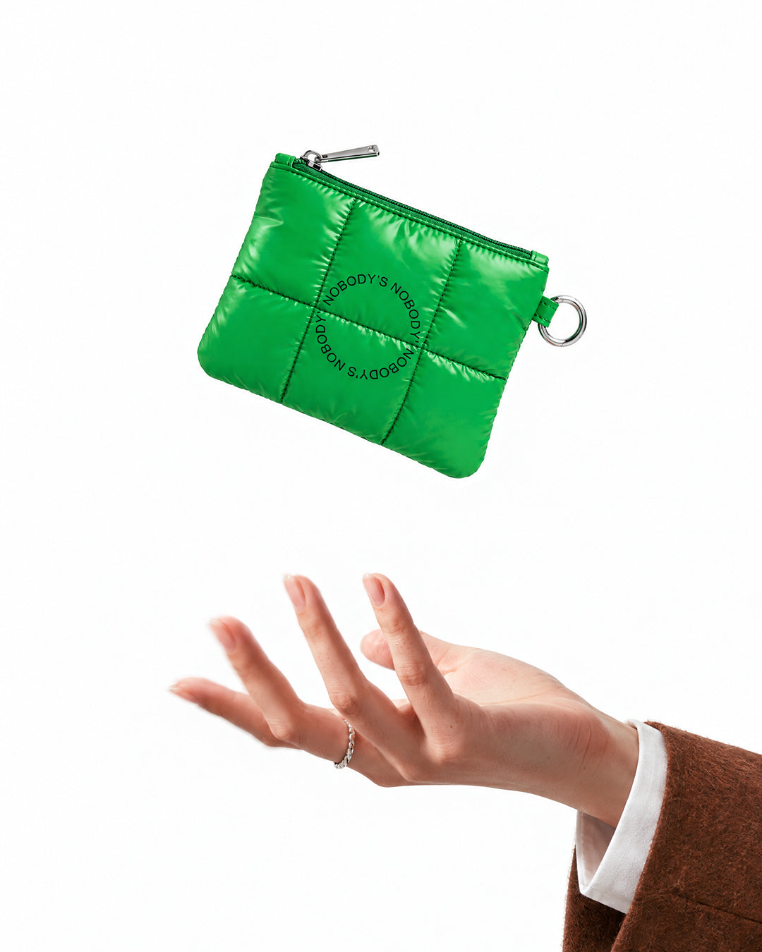 The green quilted NBDY travel pouch in the air above an open hand